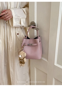 Detail of pink lychee leather bucket bag with metal buckle and cute plush bear charm