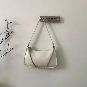 Détail du sac bandoulière blanc cassé avec chaîne argentée et logo NO FILTER sur mur épuré