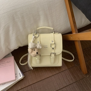 Detail of cream mini square bag with leather straps and a brown teddy bear charm