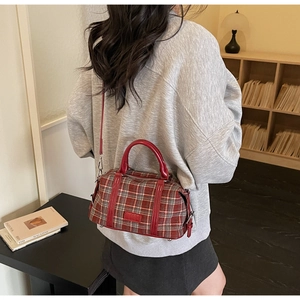 Rear view of a model carrying a vintage red-brown checkered boston bag with leather handles
