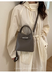 Detail of grey lychee leather bucket bag with silver twist lock on beige dress