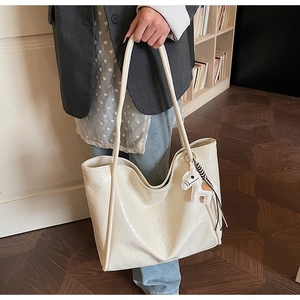 Detail of large beige glossy leather tote bag with crinkled texture and horse charm
