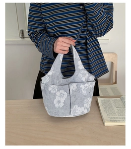 Detail of grey embroidered canvas tote bag with white floral pattern held by a model