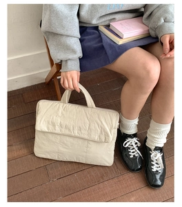 Detailed view of beige quilted laptop bag held by a model on a warm wooden floor