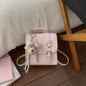 Detail of a pink square crossbody bag with decorative buckles and a plush bear charm