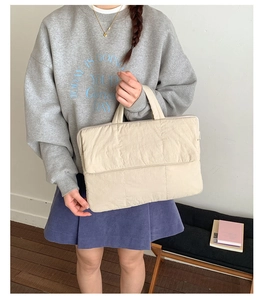Detailed view of beige quilted handbag featuring padded texture and soft top handles