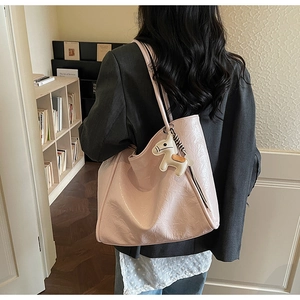 Pink minimalist tote bag with pony charm shown on shoulder in a cozy indoor setting