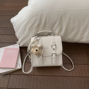 Close-up of cream square shoulder bag with silver hardware and a cute teddy bear charm