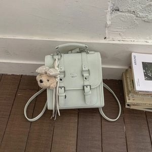 Detail of mint green flap backpack with metal buckles and cute plush bear charm