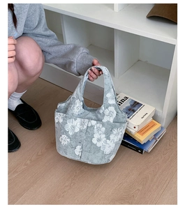 Detailed side pocket on floral grey canvas bucket bag held by a person in a minimalist room