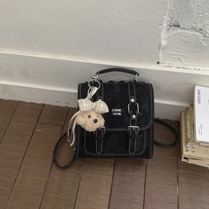 Detail of black crossbody bag with silver buckles and a cute plush dog pendant charm