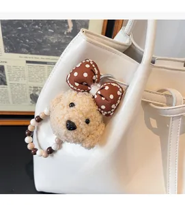 Détail d'un pendentif ours en peluche beige avec nœud sur un sac à main en cuir blanc