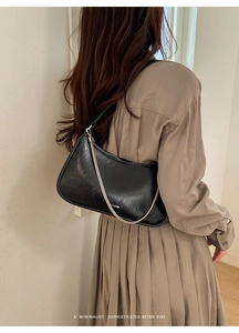 Détail du sac sous le bras en cuir noir avec chaîne argentée porté par un mannequin