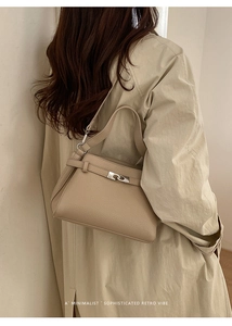 Beige leather crossbody bag with silver lock worn on a khaki trench coat for a retro vibe