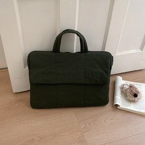 Detail view of a dark green canvas laptop bag with front flap pocket and sturdy handles