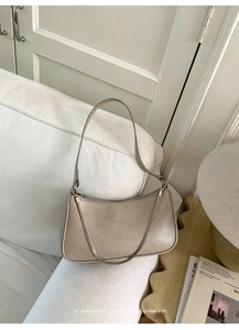 Détail d'un sac baguette beige avec chaîne argentée posé sur un canapé blanc