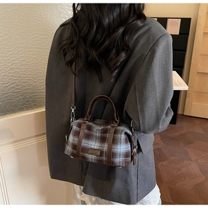 Detailed side view of vintage plaid handbag worn over a grey blazer in a cozy room