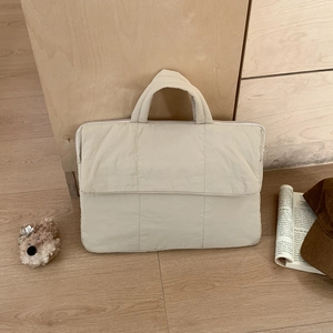 Close-up of beige quilted laptop bag with vertical stitching and cute bear keychain