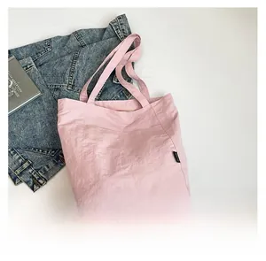 Pink tote bag with wrinkled texture nylon fabric shown with denim jacket on white background