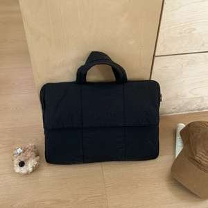 Close-up of black quilted laptop handbag with textured stripes and large front pocket