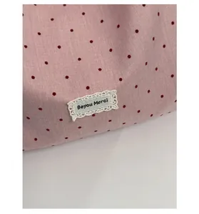 Detail shot of a floral tote bag featuring red polka dots and a lace brand tag
