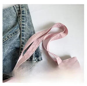 Detail view of reinforced stitching on pink fabric tote bag straps with casual denim background