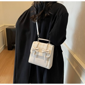 Model wearing a small cream bow backpack with beige checkerboard pattern on the flap