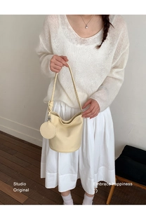Détail d'un sac seau en cuir crème avec une mini pochette ronde porté par un mannequin