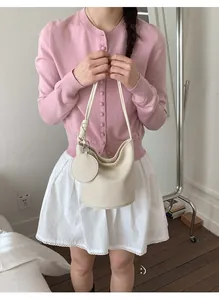 Détail d'un sac seau en cuir crème avec une bandoulière fine et un charme rond latéral