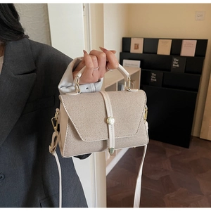 Détail du sac à main beige minimaliste montrant la texture tissée et la boucle dorée