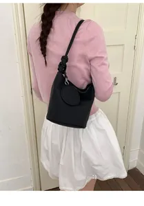 Détail d'un sac seau en cuir noir avec une bandoulière à nœud au design unique