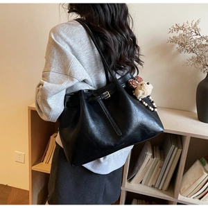 Détail d'un sac cabas en cuir mat noir avec boucle décorative et breloque ours en peluche