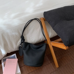 Détail du sac seau en cuir grainé noir avec bandoulière nouée et breloque ronde