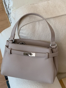 Borsa a mano minimalista in pelle taupe con chiusura argentata su un divano bianco