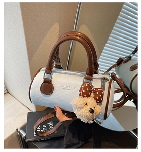 Detailed view of white barrel bag with brown handles and cute plush bear charm decoration