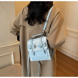 Detailed back view of a blue plaid backpack with bows on a trench coat outfit