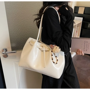 Détail d'un sac cabas en simili cuir blanc crème avec un charme de chien en peluche et perles