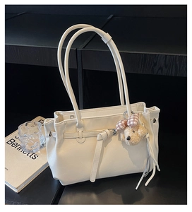 Detailed close-up of a white tote bag with a plush bear charm and leather strap accents