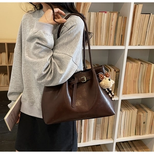 Détail d'un cabas en cuir café foncé avec boucle décorative et breloque ours en peluche