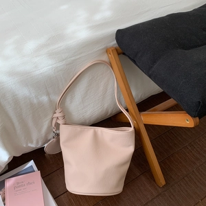 Détail du sac seau rose avec bandoulière nouée et étiquette ronde en cuir assortie