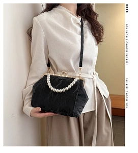 Detail of black pleated handbag featuring large pearl handle and vintage metal clasp