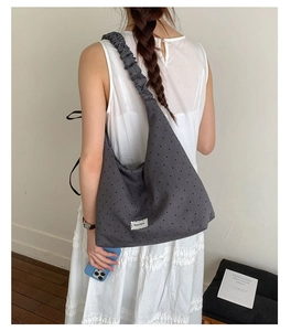 Detail of grey polka dot tote bag featuring ruffled shoulder strap and lace trim label
