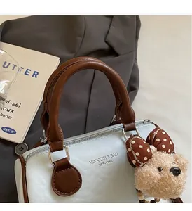 Detail of blue and white cylinder handbag with brown leather trim and a teddy bear charm