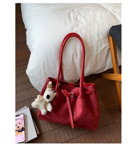 Detail of red suede tote bag with leather straps and a cute plush bear charm accessory