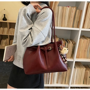 Détail d'un sac cabas bordeaux en cuir avec breloque ours en peluche dans une bibliothèque
