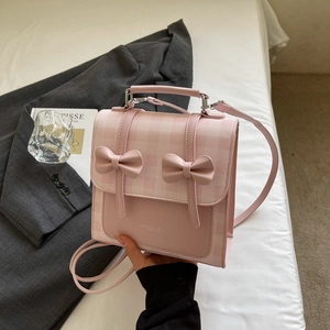 Detail view of pink plaid crossbody bag with 3D bow accents on a minimalist setting