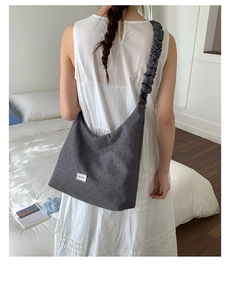Detail view of the dark grey polka dot tote bag with pleated ruffle strap on white dress