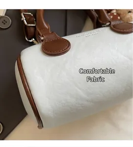 Close-up of the smooth beige leather texture and brown trim of the retro pillow bag