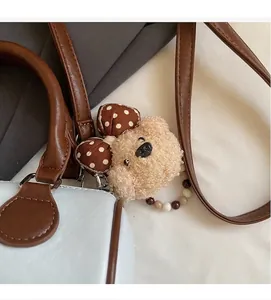 Detail of plush bear keychain with polka dot bow and beaded ring on light blue handbag