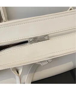 Detail view of smooth silver metal zipper and textured white leather on fashion tote bag